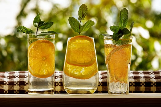 Lemon water with mint in the three glasses. Summer garden background.