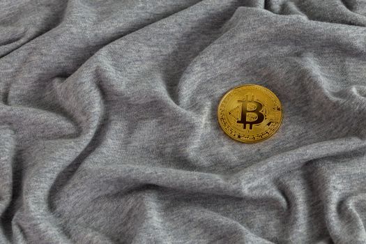 Golden bitcoin shiner on gray crumpled cotton cloth.