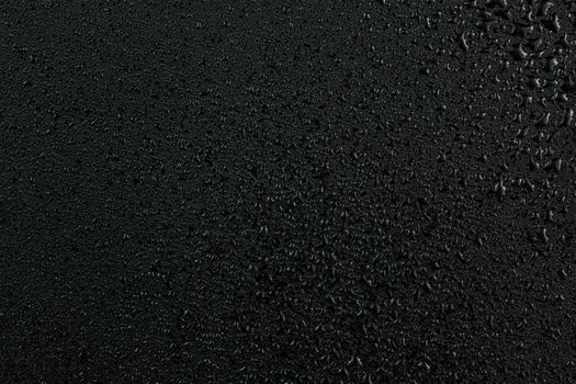 dark abstract background of water drops on flat black rubber surface