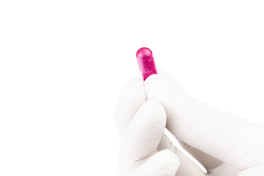 hand in medical glove holding plastic pink color organic med capsule isolated on white background closeup.