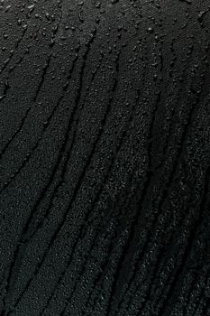 water drops on flat black rubber surface dark macro background with long smudges in vertical orientation