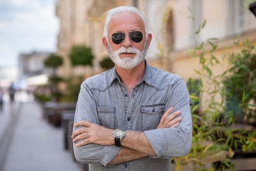 Happy rich old man with beard and sun glasses on street posing and smiling, portrait
