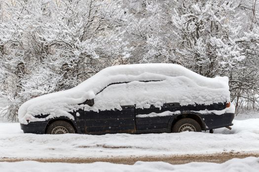 Old dirty car covered by thick snow layer with selective focus.