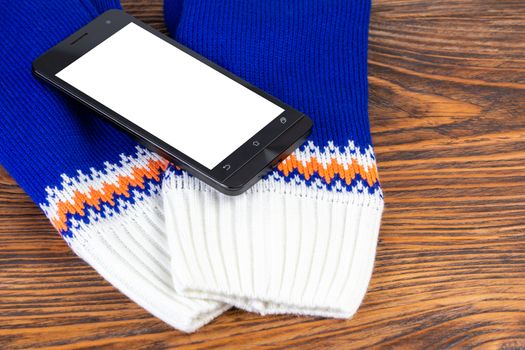 blue and white knited mittens with cellphone on wooden background.