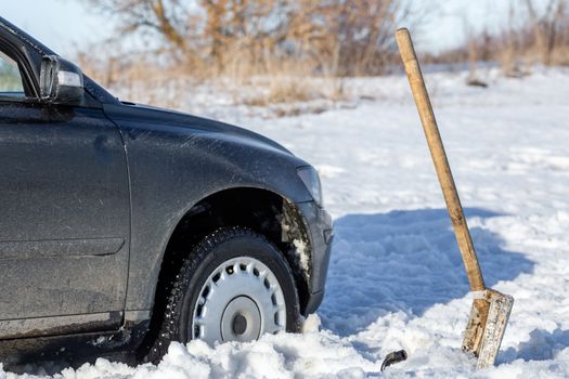 car stuck in snow offroad at daylight with shovel and selective focus.