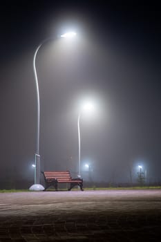 alone bench in dark night misty park with tall lights and selective focus