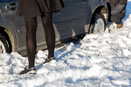 man working at car stuck in snow on knee girl just standing.