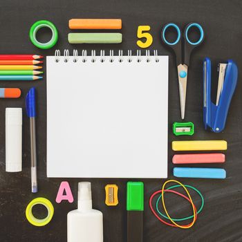 Top view on colorful stationery. Back to school flat lay concept. Blackboard background with copy space. Square aspect ratio.