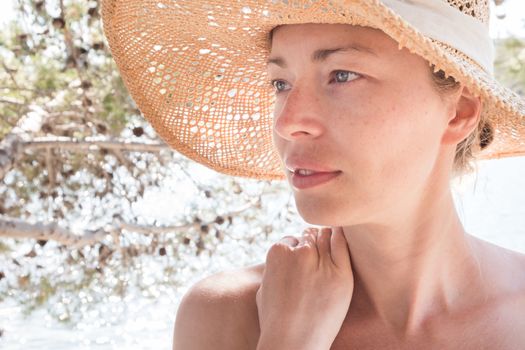 Close up portrait of no makeup natural beautiful sensual woman wearing straw sun hat on the beach in shade of a pine tree.