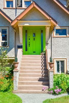 Green entrance door of snug family house under the porch with the doorsteps in front