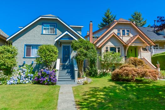 Snug warm family houses side by side. Residential house with the pathway over front yard lawn on blue sky background.