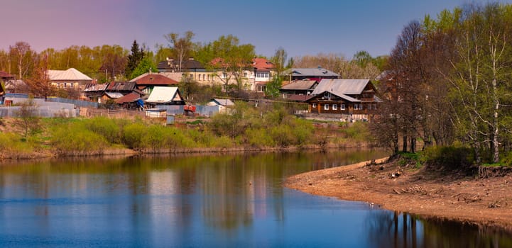 Old houses in Vologda, Russia, Europe. Blue sunset sky in background and river in foreground. Travel and architecture.