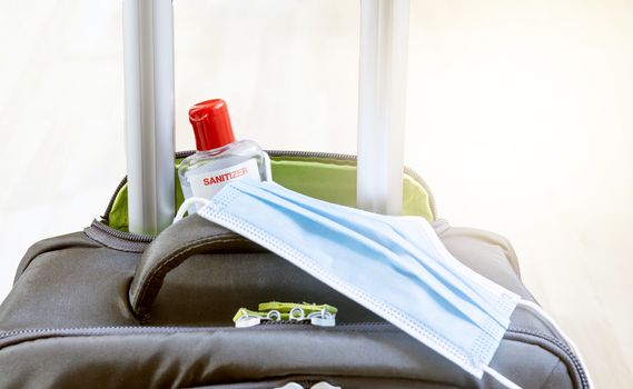 detail of a gray suitcase with a surgical mask and a bottle of hand sanitizer in the handle pocket. Travel equipment during the coronavirus pandemic