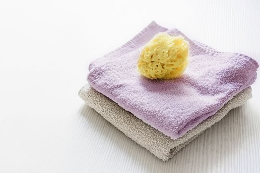A natural yellow sponge on towels stacked on a white wooden table. Personal care and hygiene. Bath and relax