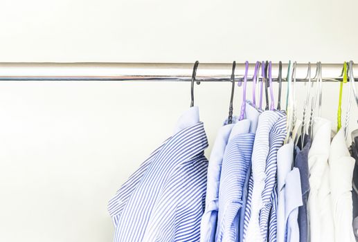 A group of men's shirts of various colors hung with hangers inside a wardrobe. Fashion and clothes.