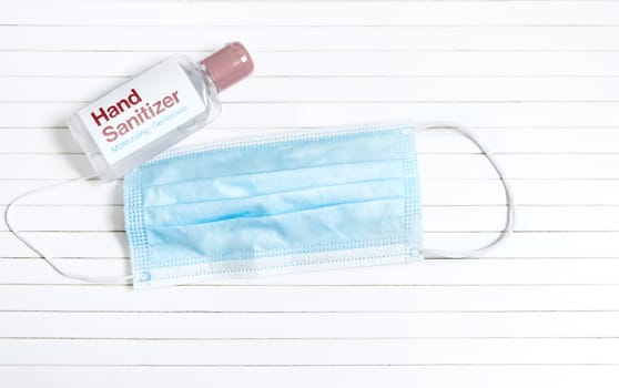 a plastic bottle containing hand sanitizing gel next to a celestial surgical mask on a white striped background. Prevention and sanitation