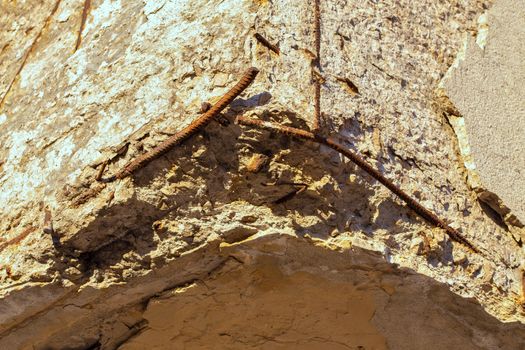 Old damaged reinforced concrete corner under direct orange sunlight with bare rusted steel skeleton. Selective focus technique.