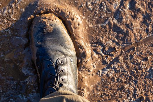 army boot in wet mud closeup top-down vew with selective focus at daylight.