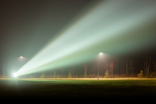 big backlight projector or spotlight in foggy night park with huge light beam at summer