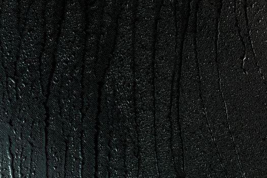 water drops on flat black rubber surface dark macro background with long smudges