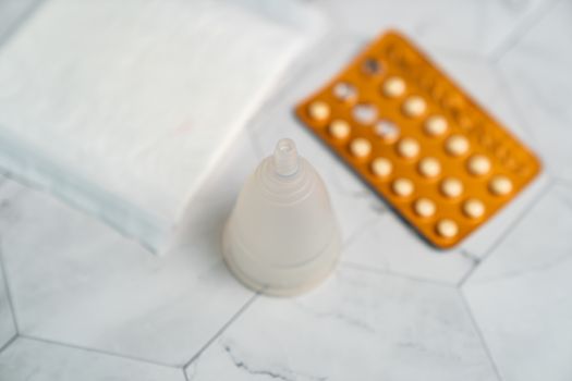 Birth control pill,sanitary napkins and menstrual cups with on white marble background.