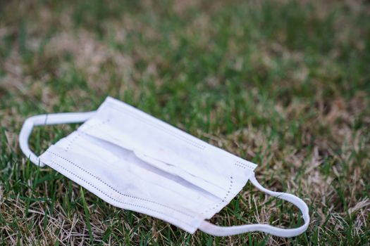 Used dirty face surgical mask dropped on the ground, selective focus center mask