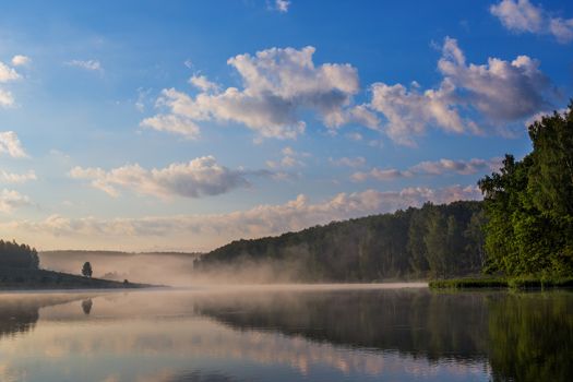 foggy flatland riverside at summer sunrise with trees