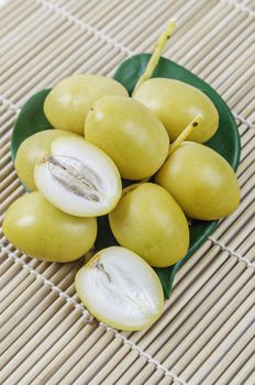 A bunch of fresh date palm fruits with green leaf on bamboo mat.