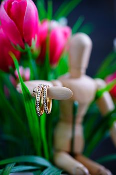 Wooden figure holding two golden wedding ring resting with fake pink tulip flower