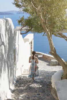 Back side of woman tourist walking on stairs in Oia village, Santorini with the mediterranean sea. Santorini Europe summer destination.