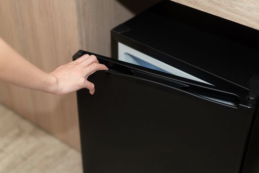 Woman hand opening refrigerator door on wooden floor.