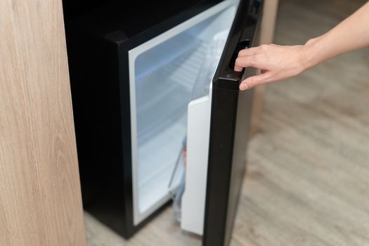 Woman hand opening refrigerator door on wooden floor.