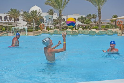 Father and sons having fun playing water polo in tropical hotel resort swimming pool on vacation