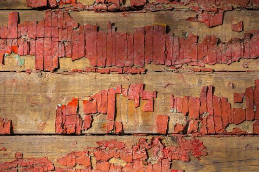 Closeup shot of peeling faded red paint on horizontal wooden planks under direct sunlight