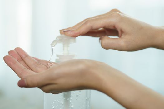 Female hands using wash hand sanitizer gel pump dispenser. Clear sanitizer in pump bottle, for killing germs, bacteria and virus.