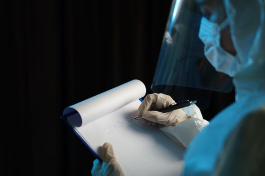 Woman wearing protective hazmat suit (PPE) and writing virus infected patient's laboratory report.