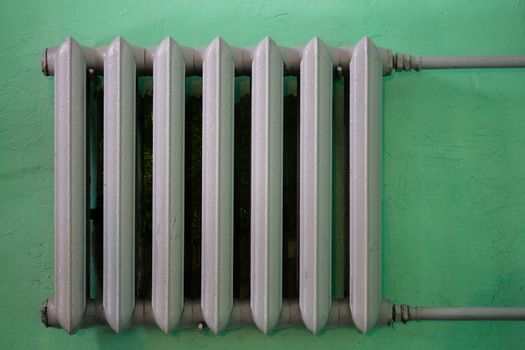 gray painted cast iron water radiator on green wall.