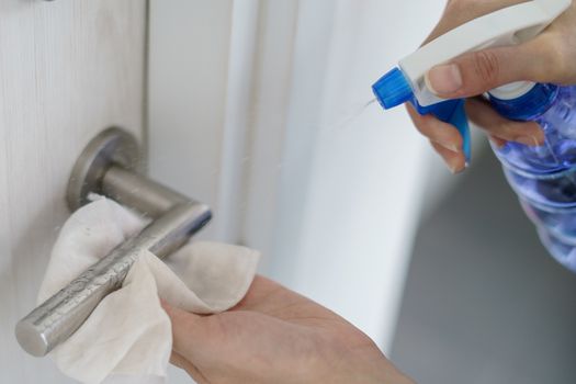 Woman hand using napkin and detergent spray cleaning doorknob for corona virus or Covid-19 protection.