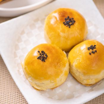 Tasty baked egg yolk pastry moon cake for Mid-Autumn Festival on bright wooden table background. Chinese festive food concept, close up, copy space.