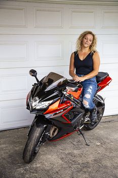 twenty something blond hair woman, falling asleep on top of sport motocycle, in a front of a garage door
