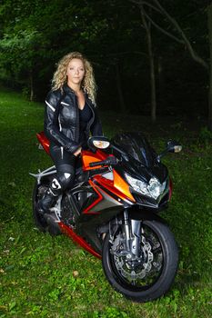 twenty something blond hair woman, wearing motocyle clothes, sitting on top of sport motocycle, in a park