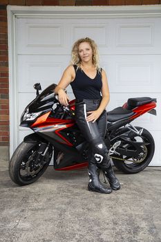 twenty something blond hair woman, hanging out on a sport motocycle, in front a of garage door
