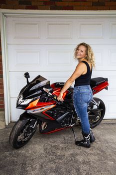 blond woman, in her twenties, with a sport motocycle, in front of a garage door