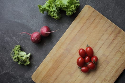 Tomatoes on a cutting board on a gray table and fresh vegetables, lettuce, broccoli, radish