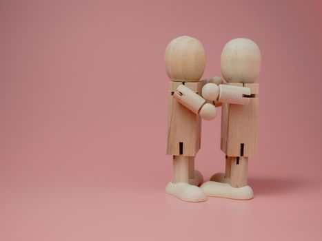 2 wooden dolls hugging each other on a pink background.
Concept of social contact from wooden dolls.