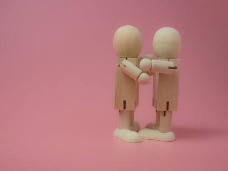 2 wooden dolls hugging each other on a pink background.
Concept of social contact from wooden dolls.