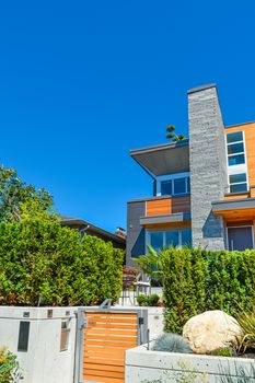 Entrance of new luxury family house with landscaped front yard. Modern residential house with concrete terrace and wooden gate