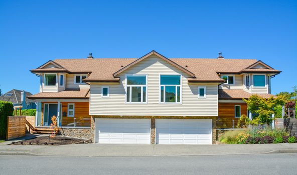 Brand new residential duplex house for two families. House for sale on blue sky background. Duplex house with wide garage doors along the road in the front