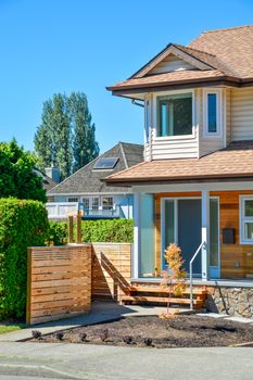Main entrance of brand new family house in suburban. House for sale on blue sky background. Residential house with porch over the entrance door and concrete pathway over the front yard.
