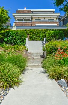 Concrete pathway with stairs to residential house on the trarrace over landscaped front yard